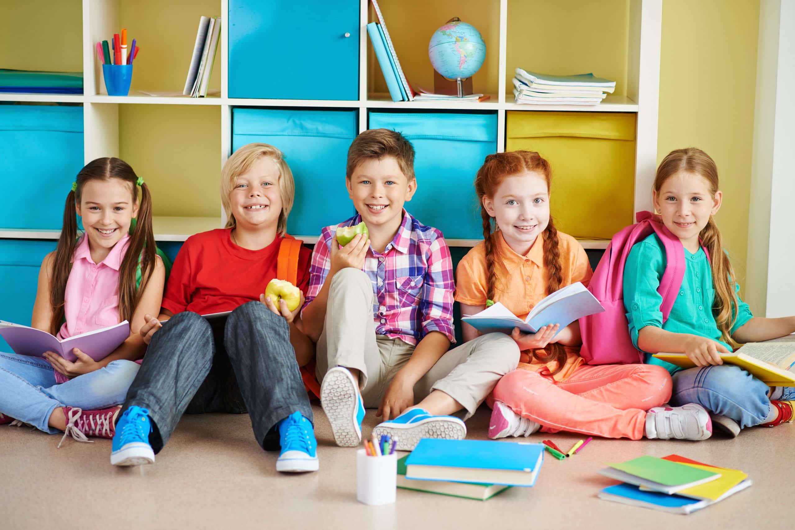 Cute friends sitting on the floor of classroom and doing schoolwork